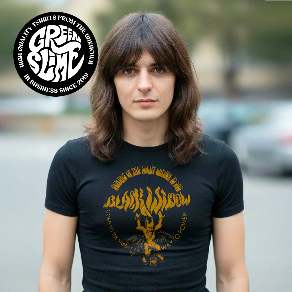A person with shoulder-length brown hair wears a fitted black T-shirt with a vintage mustard-gold “BLACK WIDOW” graphic and a small devil figure, plus circular text reading “Demons of the Night Gather to See • Come to the Sabbat • Way to Power.”